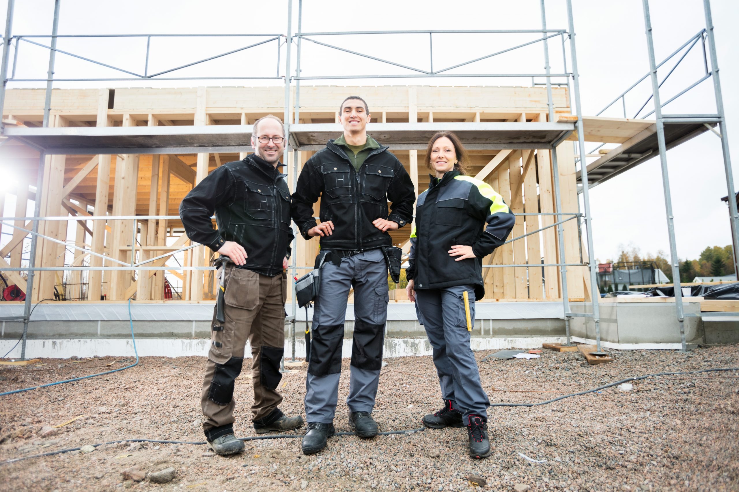 Low angle portrait of male and female carpenters standing with hands on hips at construction site